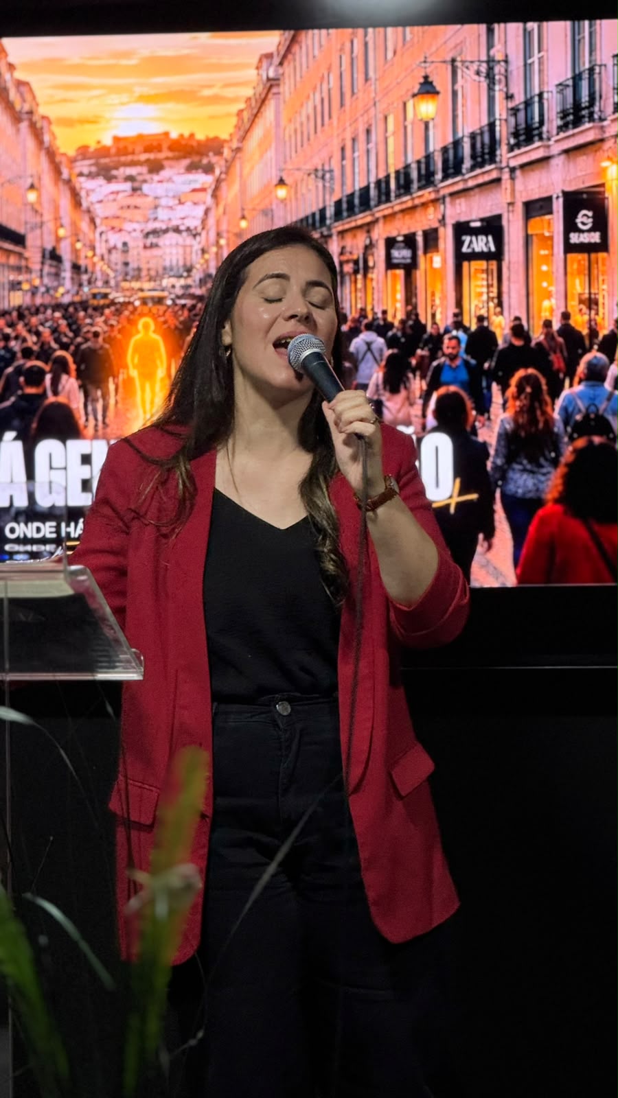 Mulher de casaco vermelho a cantar, de olhos fechados