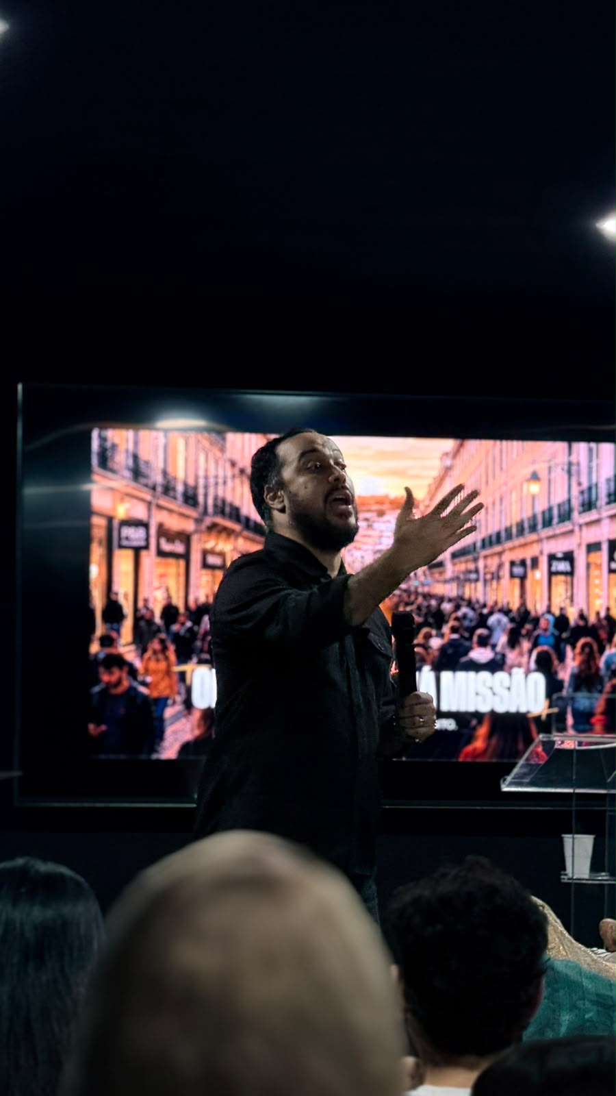 Pregador de braço estendido, com uma rua de Lisboa no ecrã atrás